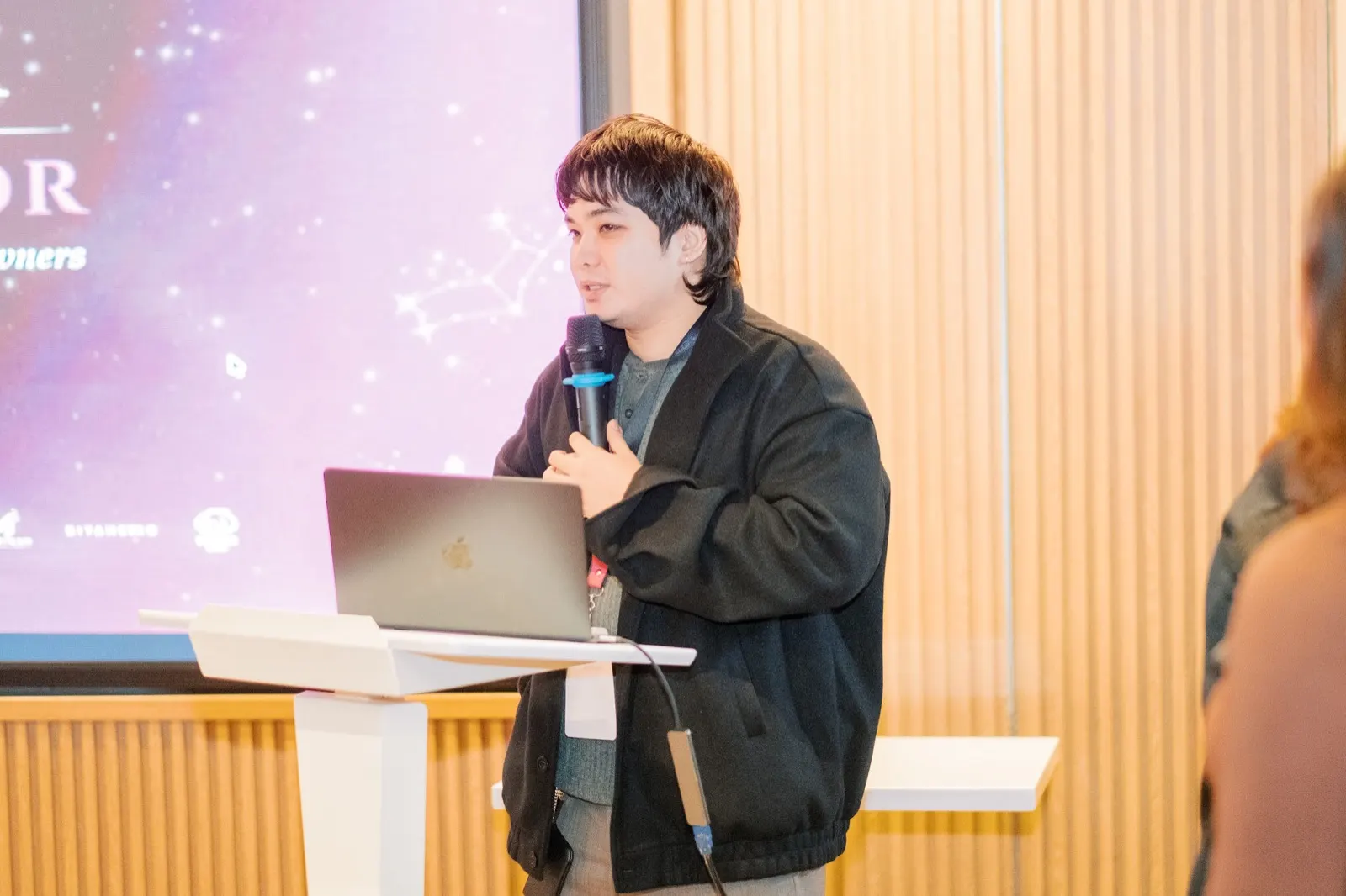 Jamz Jamorol speaking at a podium with a microphone, laptop open in front of him